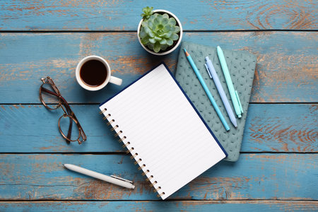 Notebooks with eyeglasses and cup of tasty coffee on blue wooden backgroundの写真素材
