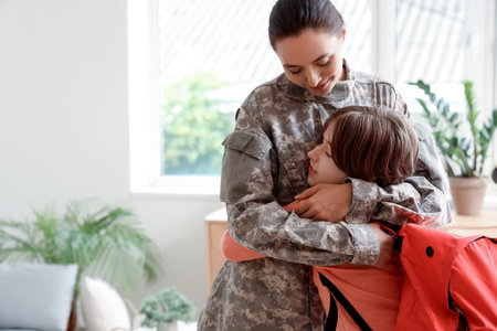 Military mother hugging and getting her little son ready for school in living room