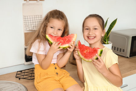 Happy little girls eating fresh watermelon at table in kitchenの写真素材