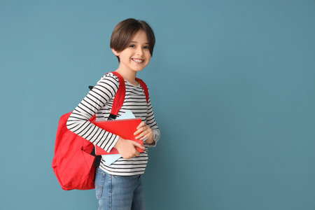 Happy little boy with backpack and notebooks on blue backgroundの写真素材