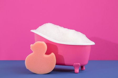 Small bathtub with soap foam and sponge on color backgroundの写真素材
