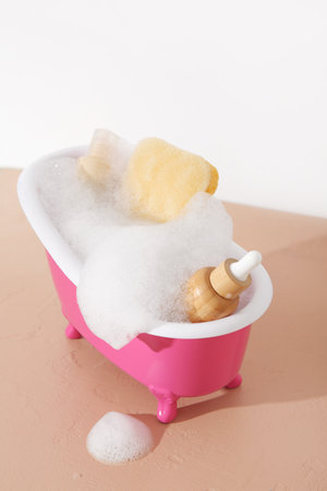 Small bathtub with foam, cosmetic products and sponge on color table against light backgroundの写真素材