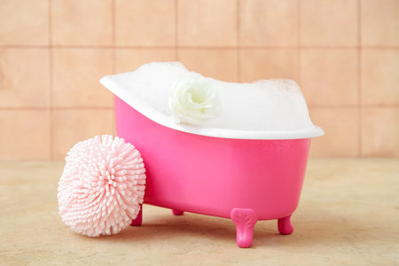 Small bathtub with soap foam and sponge on color backgroundの写真素材