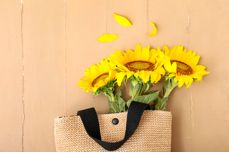 Stylish straw bag with beautiful sunflowers on beige wooden backgroundの写真素材