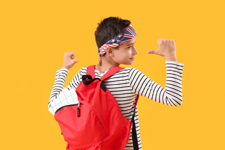 Fashionable schoolboy pointing at red backpack on orange backgroundの写真素材