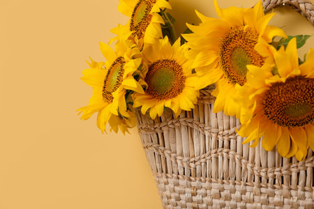 Stylish straw bag with beautiful sunflowers on yellow backgroundの写真素材