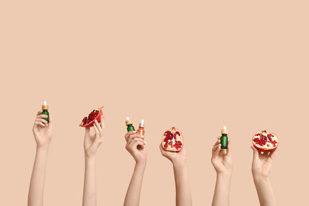 Female hands holding cosmetic products and pomegranate on beige backgroundの写真素材