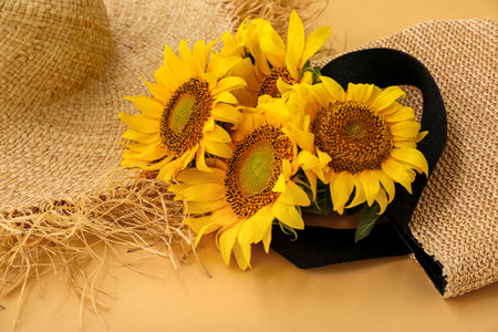 Stylish straw bag with hat and beautiful sunflowers on orange backgroundの写真素材