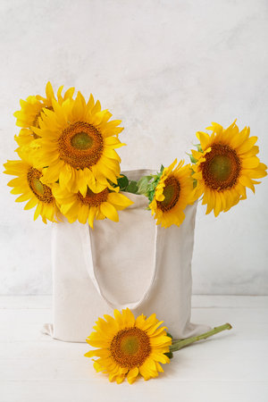 Eco bag with beautiful sunflowers on white wooden tableの写真素材