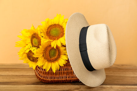 Wicker basket with hat and beautiful sunflowers on wooden tableの写真素材