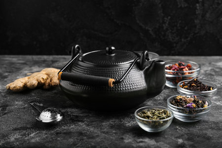 Composition with teapot, different types of tea and infuser on dark tableの写真素材