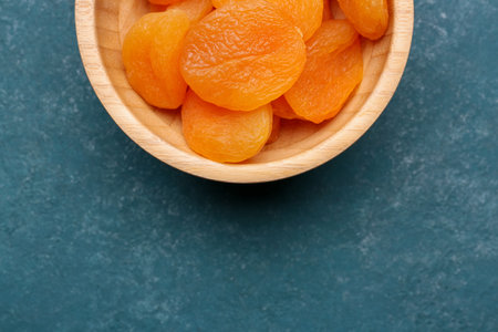 Wooden bowl with tasty dried apricots on blue backgroundの写真素材