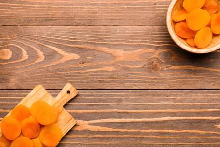 Board and bowl with tasty dried apricots on wooden backgroundの写真素材