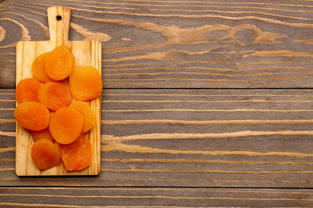 Board with tasty dried apricots on wooden backgroundの写真素材