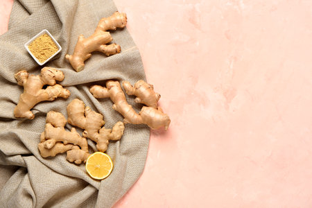 Fresh ginger roots, half of lemon and bowl of dried powder on pink backgroundの写真素材