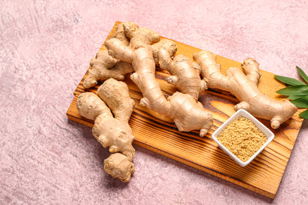 Wooden board with fresh ginger roots and bowl with dried powder on pink backgroundの写真素材