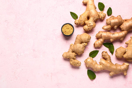 Fresh ginger roots with leaves and bowl of dried powder on pink background