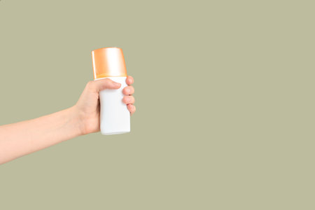 Female hand with bottle of sunscreen cream on green backgroundの写真素材