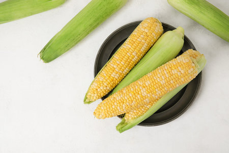 Plate with fresh corn cobs on light background