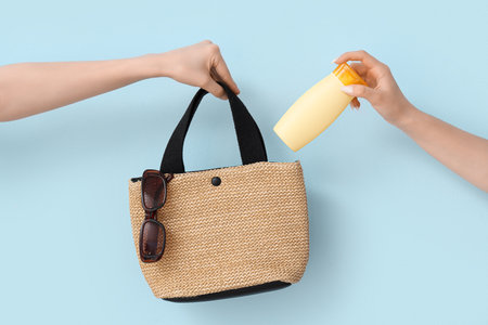 Female hands with bottle of sunscreen cream and bag on blue backgroundの写真素材