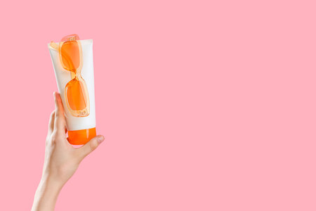 Female hand with bottle of sunscreen cream and sunglasses on pink backgroundの写真素材