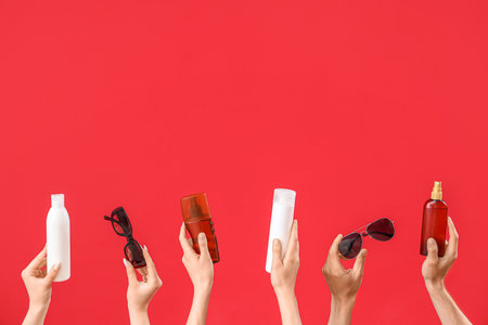 Female hands with bottles of sunscreen cream and sunglasses on red backgroundの写真素材