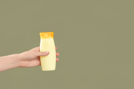 Female hand with bottle of sunscreen cream on green backgroundの写真素材