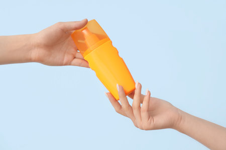Female hands with bottle of sunscreen cream on blue backgroundの写真素材