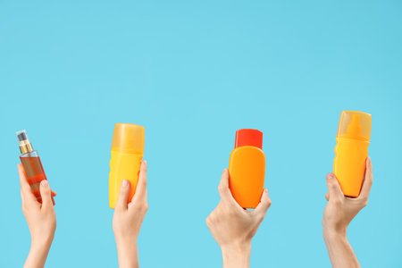Female hands with bottles of sunscreen cream on blue backgroundの写真素材