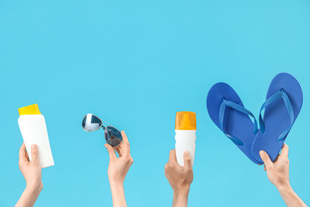 Female hands with bottles of sunscreen cream, sunglasses and flip flops on blue backgroundの写真素材