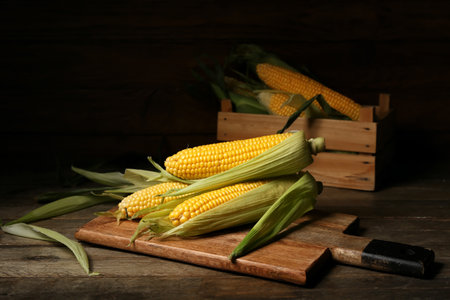 Board and box with fresh corn cobs on wooden tableの写真素材