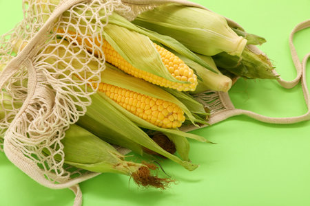 String bag with fresh corn cobs on green backgroundの写真素材