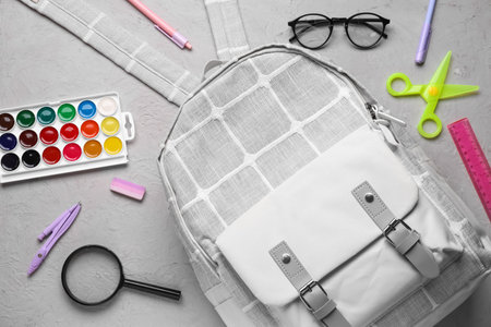 Gray school backpack with eyeglasses, magnifying glass and different stationery on grunge backgroundの写真素材