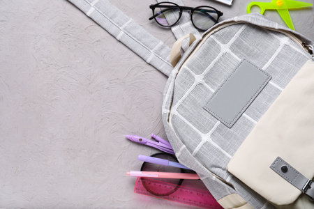 Gray school backpack with eyeglasses, magnifying glass and different stationery on grunge backgroundの写真素材