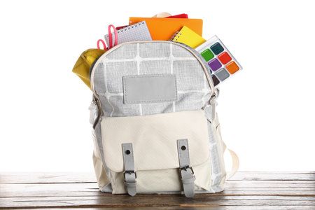 Gray school backpack with notebooks, watercolors and scissors on wooden table near white backgroundの写真素材
