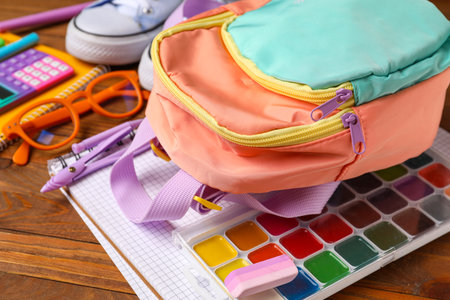 Colorful school backpack with eyeglasses, watercolors and different stationery on wooden tableの写真素材