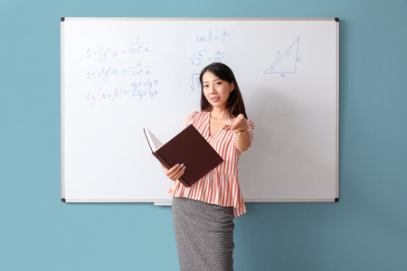 Asian Math teacher with book near flipboard in classroomの写真素材