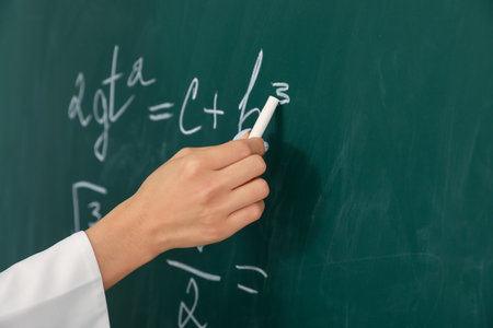 Female teacher writing Math formula on chalkboard in classroom, closeupの写真素材