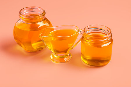 Jars and gravy boat of sweet honey on pink backgroundの写真素材