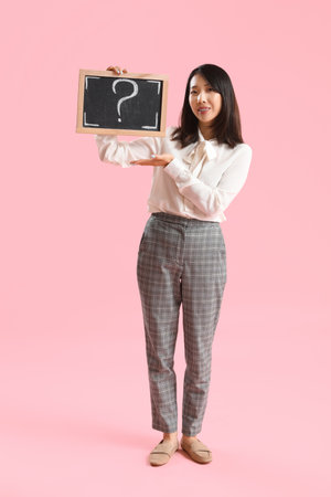 Female Asian teacher holding chalkboard with question mark on pink backgroundの写真素材
