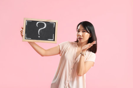 Female Asian teacher holding chalkboard with question mark on pink backgroundの写真素材