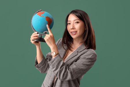 Asian Geography teacher pointing at globe on green backgroundの写真素材