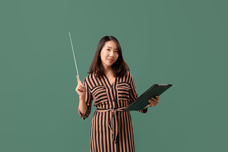 Female Asian teacher with pointer and clipboard on green backgroundの写真素材