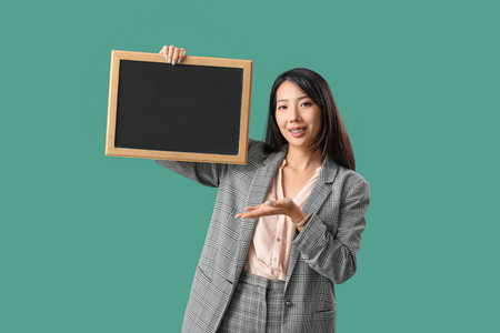 Female Asian teacher with chalkboard on green backgroundの写真素材
