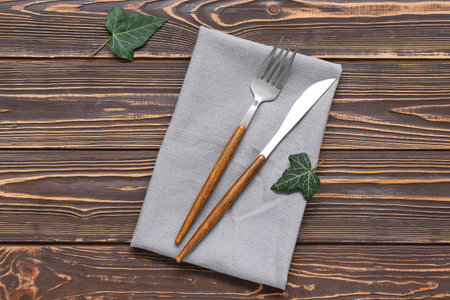 Modern silver cutlery with napkin on brown wooden background