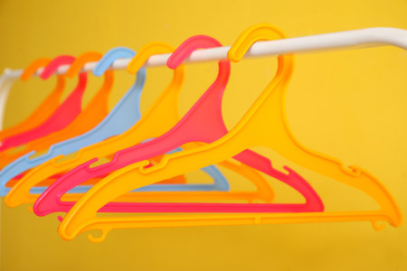 Rack with plastic clothes hangers on yellow backgroundの写真素材