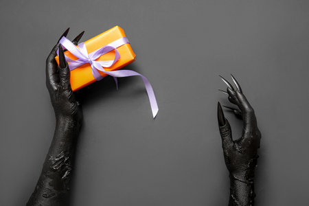 Black hands of witch with gift box on gray background. halloween celebrationの写真素材