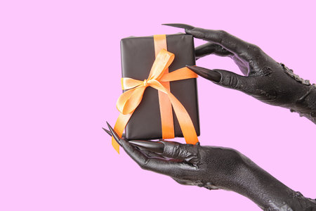 Black hands of witch with gift box on purple background, closeup. halloween celebration