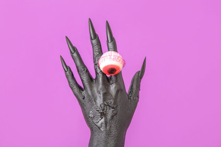 Black hand of witch with eye on purple background, closeup. halloween celebration