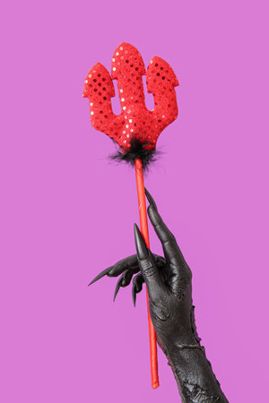 Hand of witch with red devil pitchfork on purple background. halloween celebration